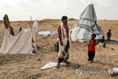 A man and children stand outside a tent at a camp for the displaced damaged by torrential rains in the Jarrahi district of Yemen's war-ravaged western province of Hodeida on August 19, 2022. (Photo by Khaled Ziad / AFP)